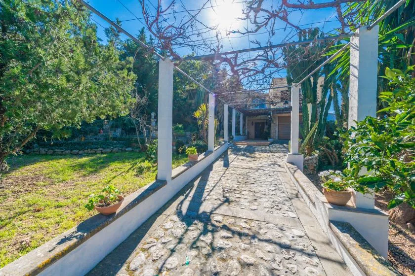 A stone garden walkway passes between white posts and leafy plants.