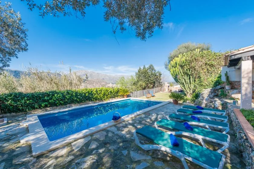 An outdoor swimming pool beside sun loungers, with trees and hills in the background.