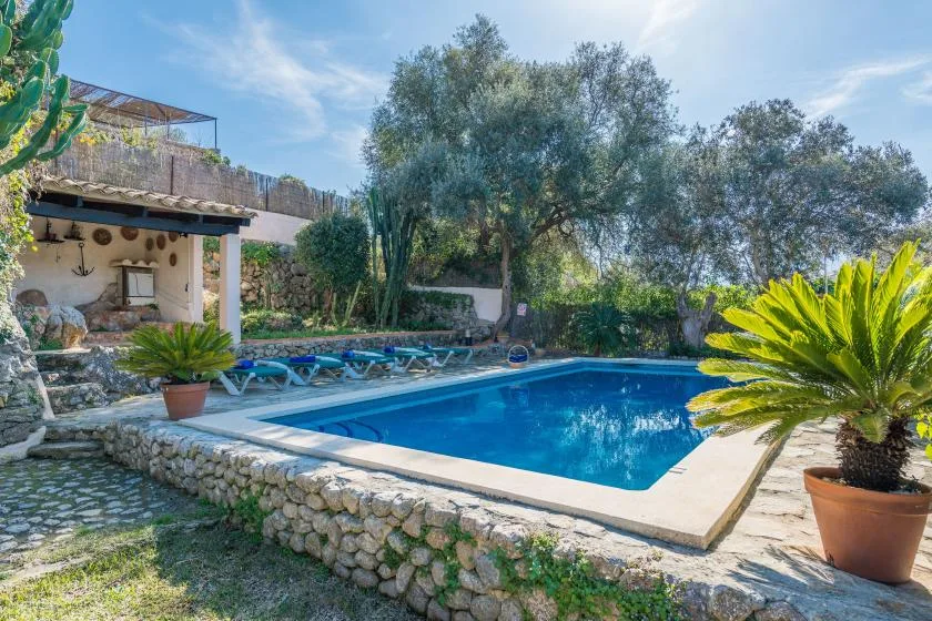Una piscina al aire libre está rodeada de árboles, muros de piedra y plantas en macetas.