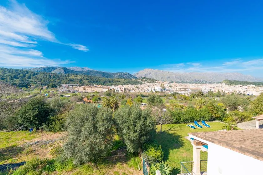 A broad landscape view shows green trees, distant buildings, and mountains beneath a clear sky.