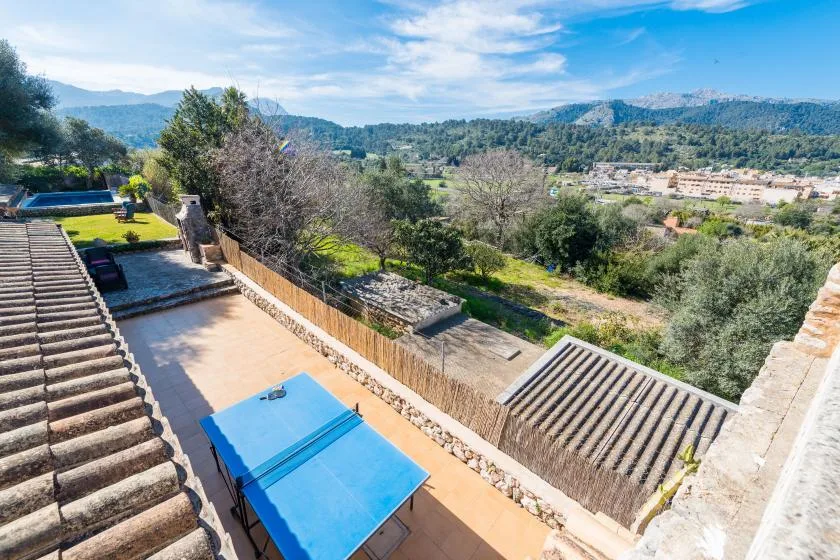 A terrace overlooks a green valley and distant hills, with a blue canopy nearby.