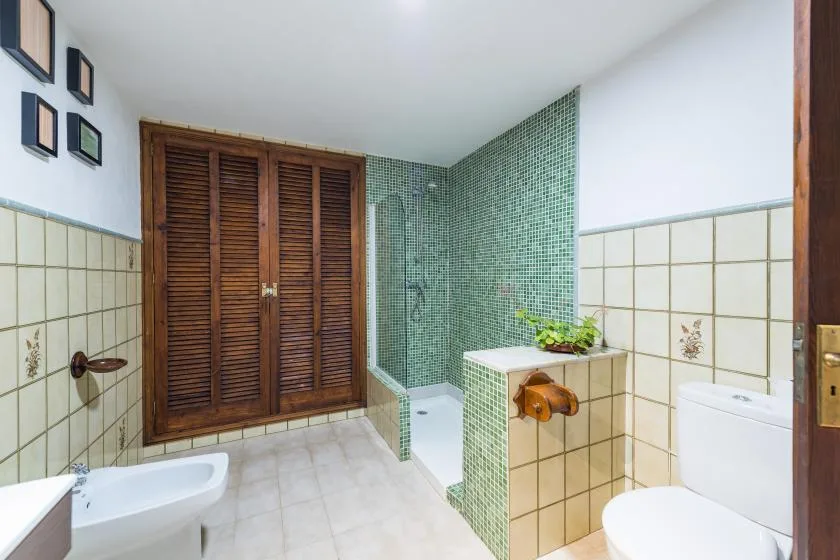 A tiled bathroom with a shower, sink, and wooden louvered closet doors.