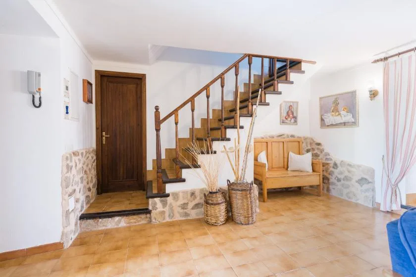 A bright entry area features a wooden staircase, a dark door, and a small seating area.