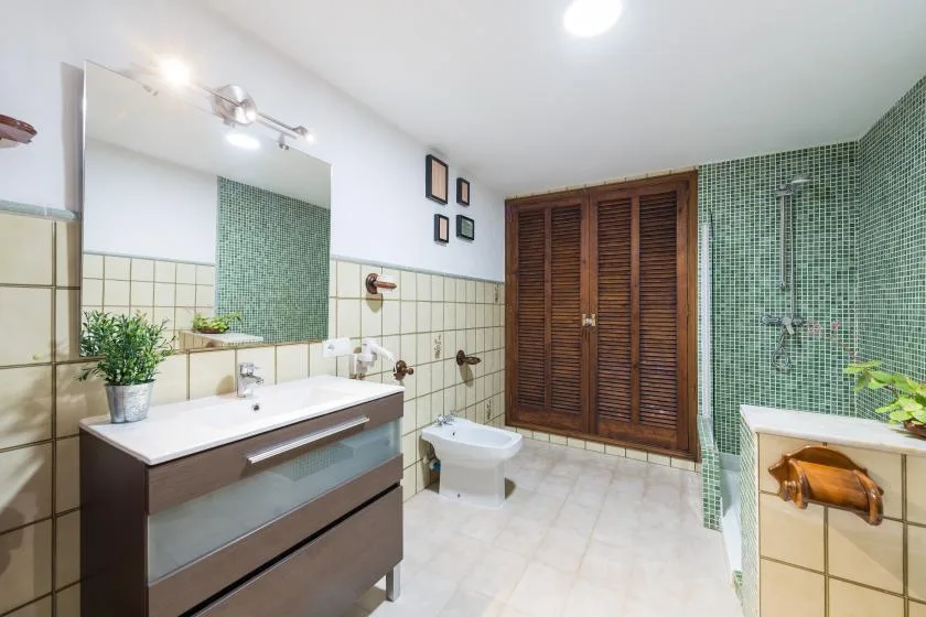 A tiled bathroom with a wide vanity, mirror, and wooden louvered doors.