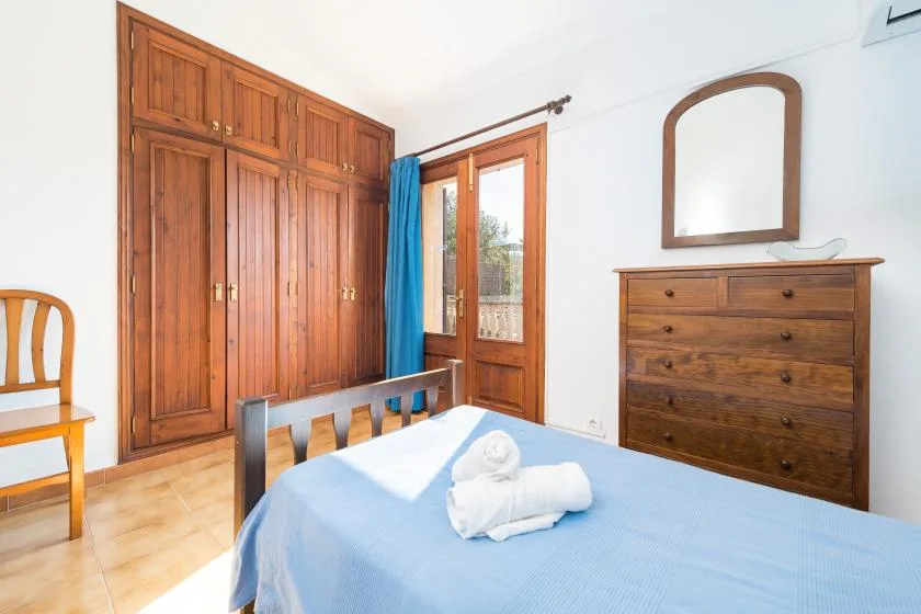 A bedroom with a blue-covered bed, wooden wardrobe, and chest of drawers.