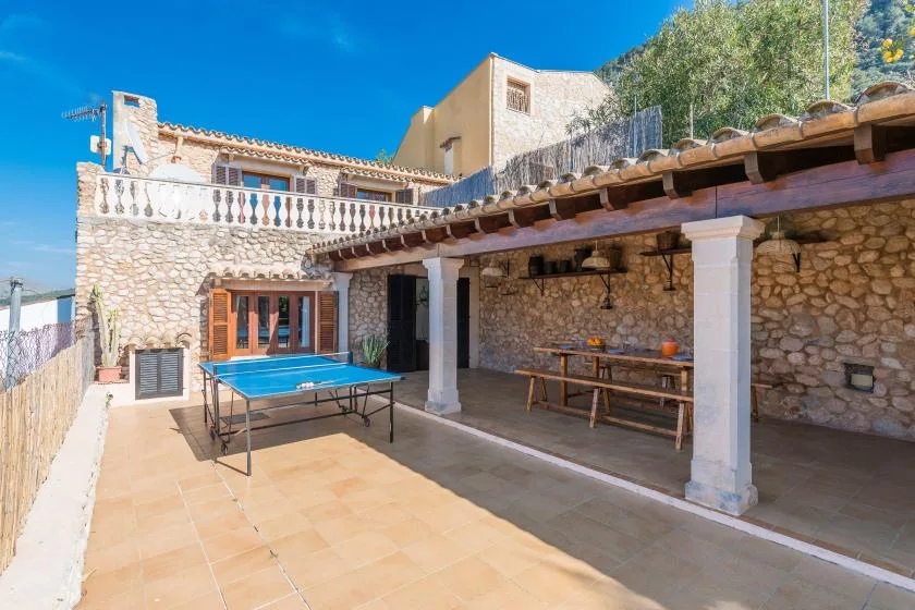Un patio de piedra cuenta con una mesa de ping-pong y una zona de comedor exterior a la sombra.