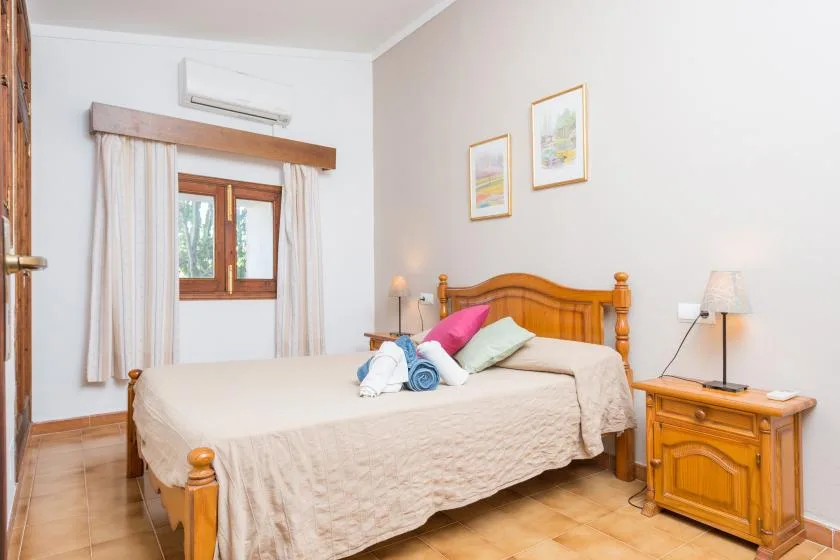 A bedroom with a wooden bed, light bedding, and a window.