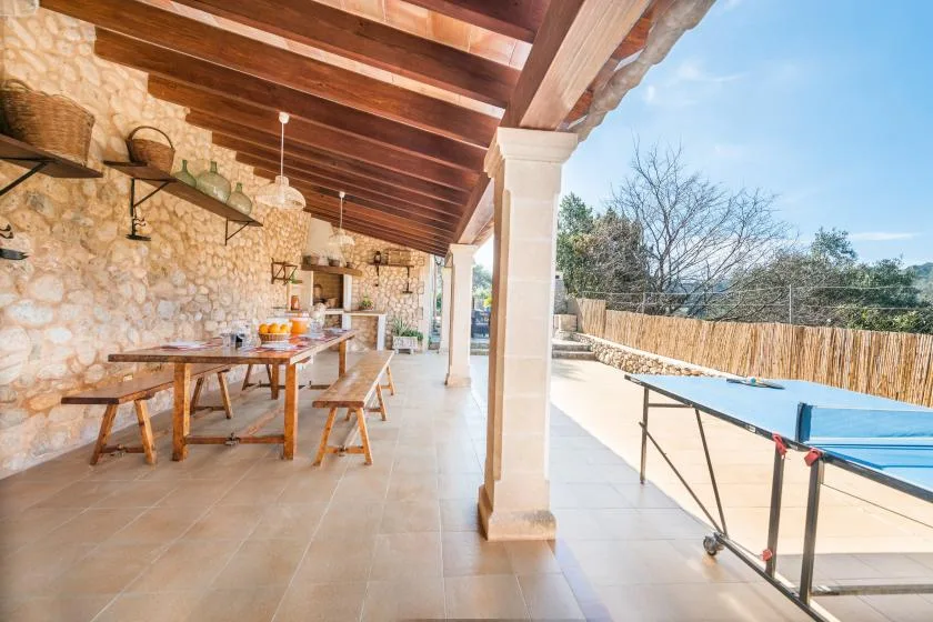 A covered outdoor dining area beside a swimming pool, with a long table and seating.
