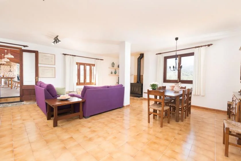A bright living and dining room with purple seating and a wooden dining table.