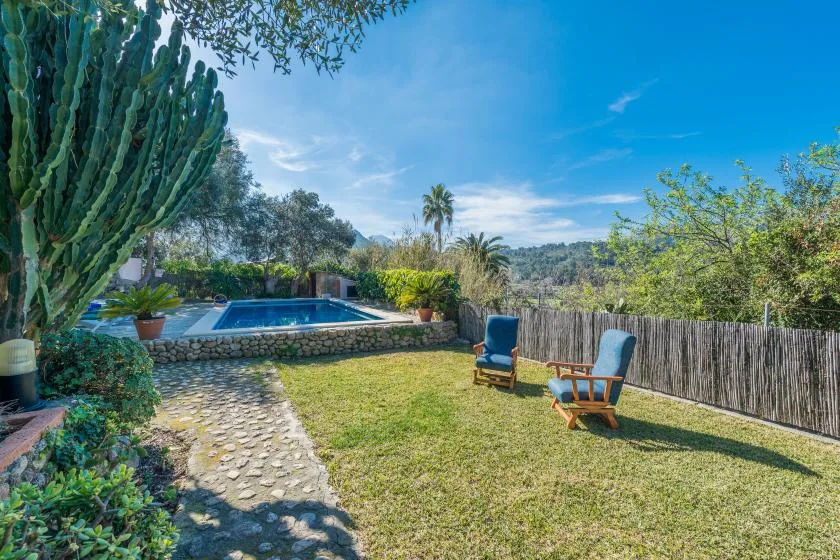 Un jardín soleado con piscina, césped y asientos al aire libre.