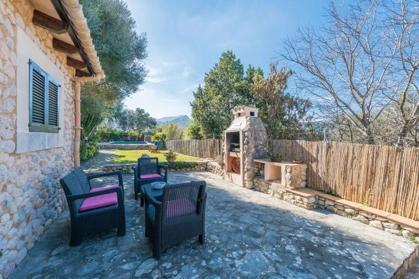 A stone patio with outdoor seating and a built-in barbecue overlooks a fenced yard.
