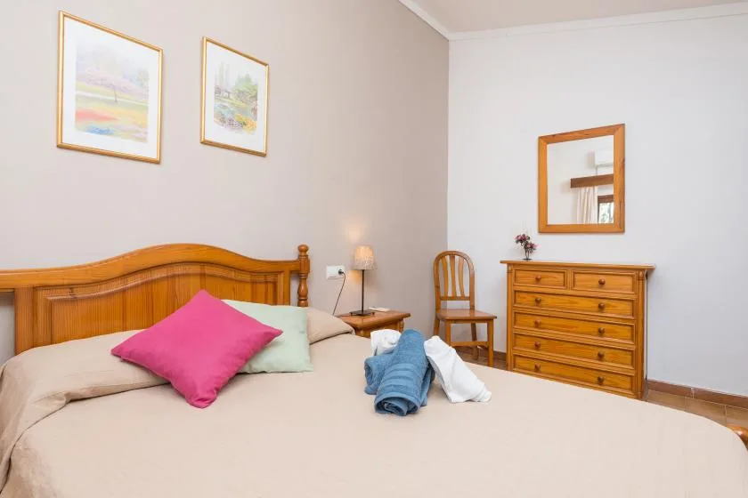 A bedroom with a wooden bed, colorful pillows, and a dresser.