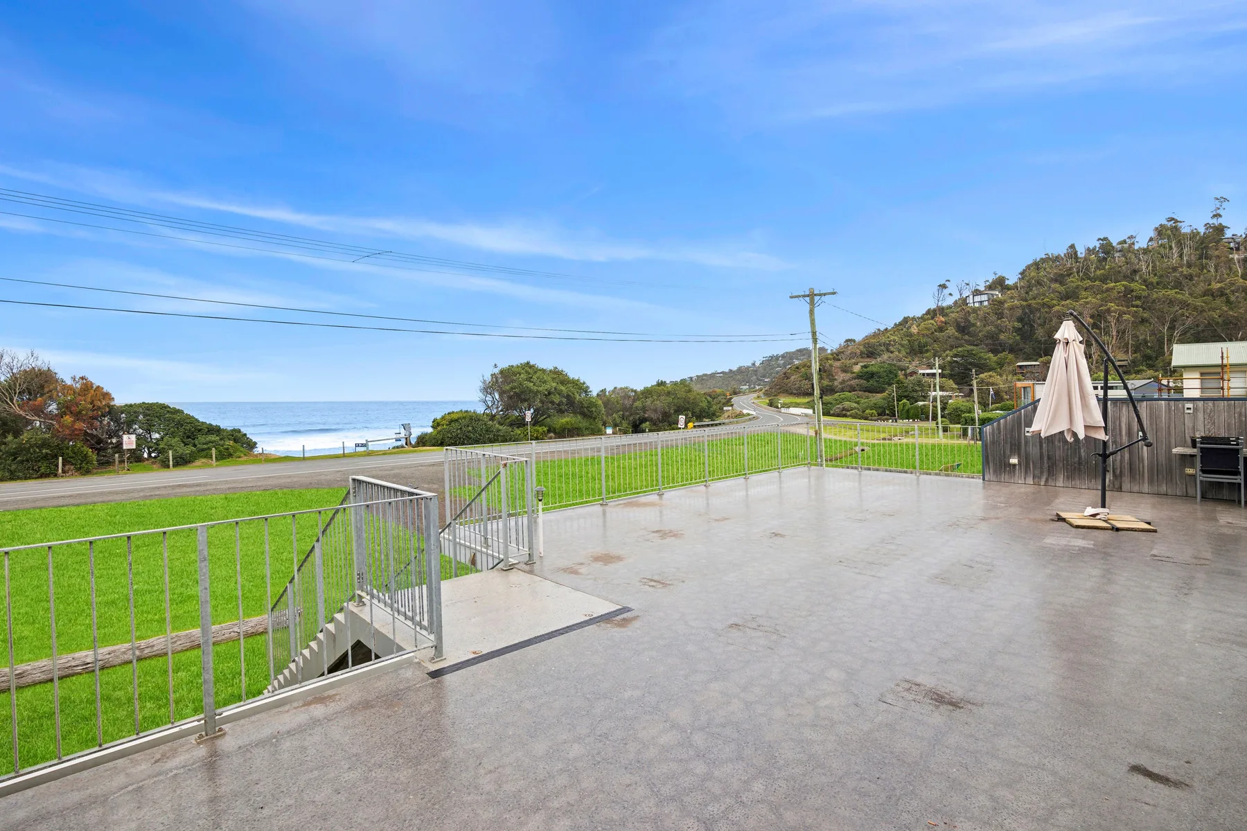 Una terraza exterior pavimentada da a una zona de césped, una carretera y el océano.