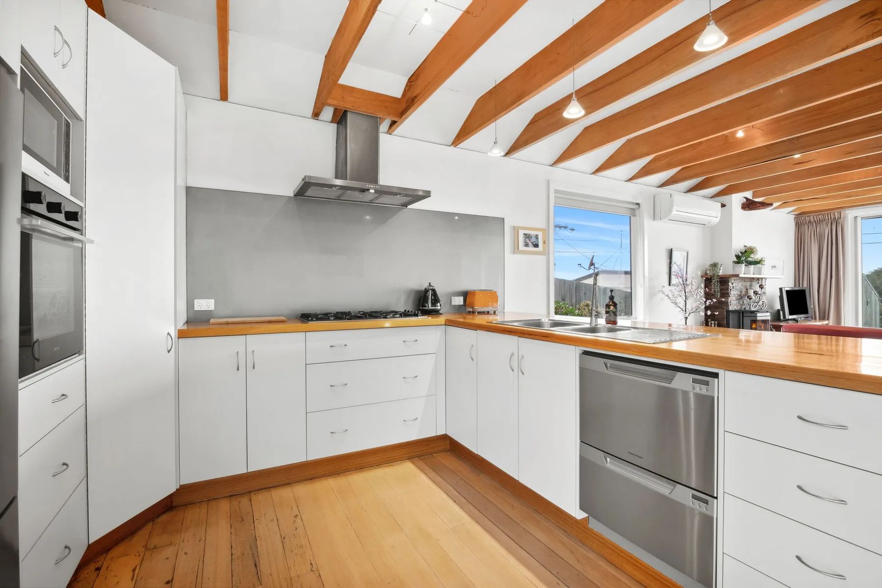Una cocina luminosa con gabinetes blancos y vigas de madera expuestas en el techo.