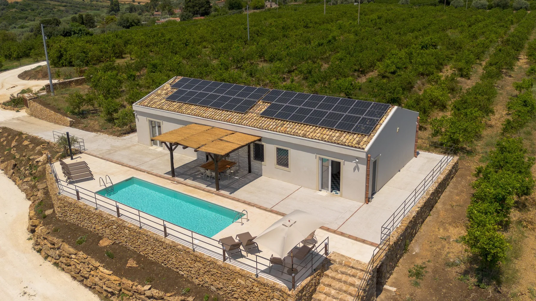 Edificio moderno de una planta con paneles solares en el techo junto a una piscina rectangular.