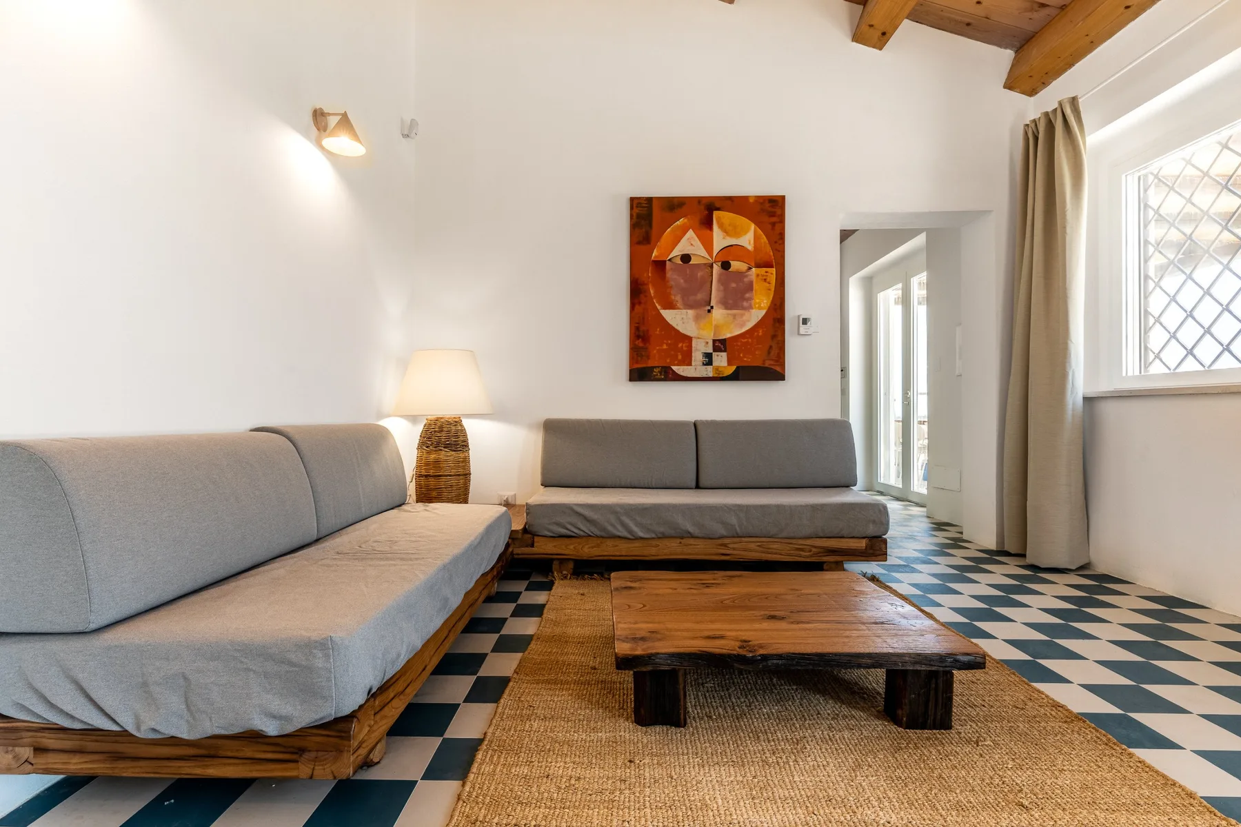 Una sala luminosa con asientos grises, una mesa de centro de madera y suelo geométrico de colores.