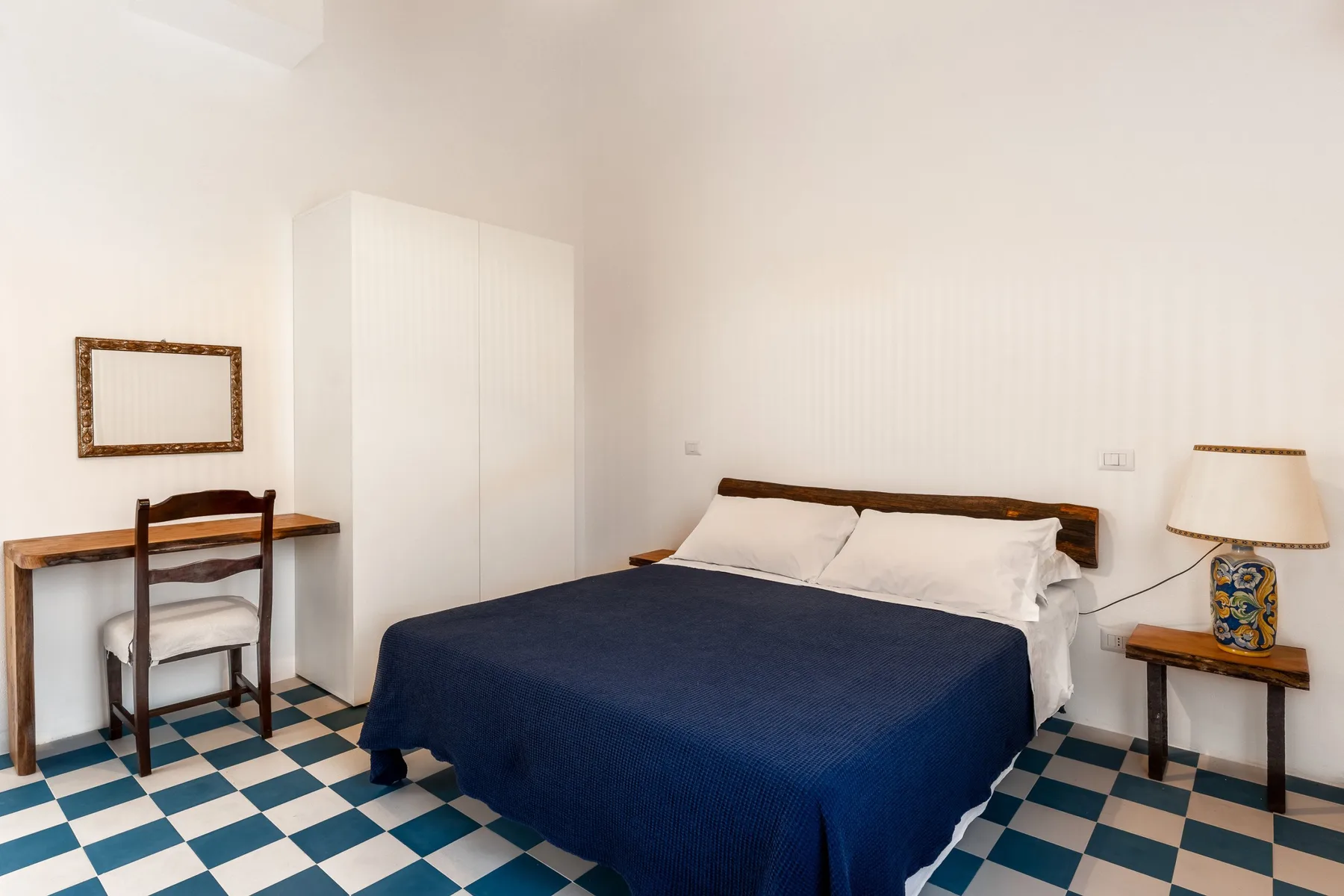 Un dormitorio con una cama cubierta con ropa de cama azul oscuro y un pequeño escritorio.