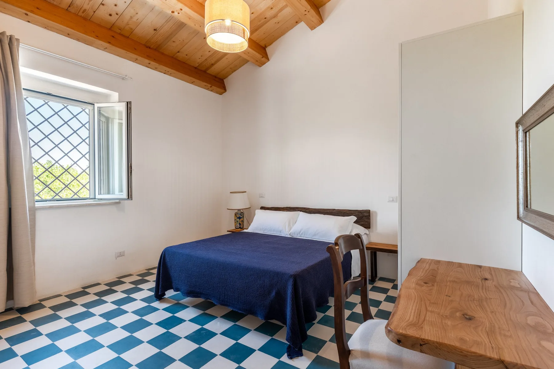 Un dormitorio con una cama, una ventana y una mesa de madera.