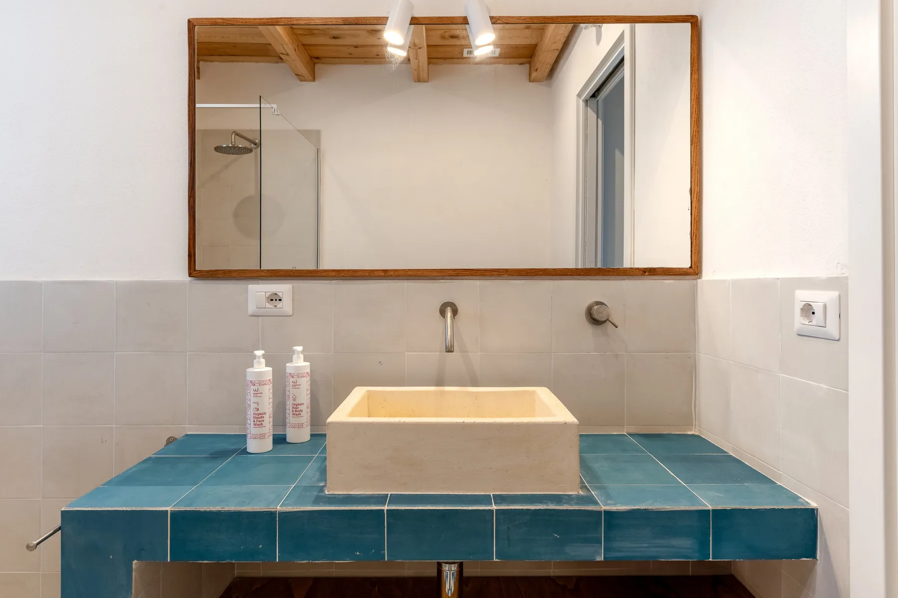 Un lavabo de baño con una pila rectangular está bajo un gran espejo de pared.