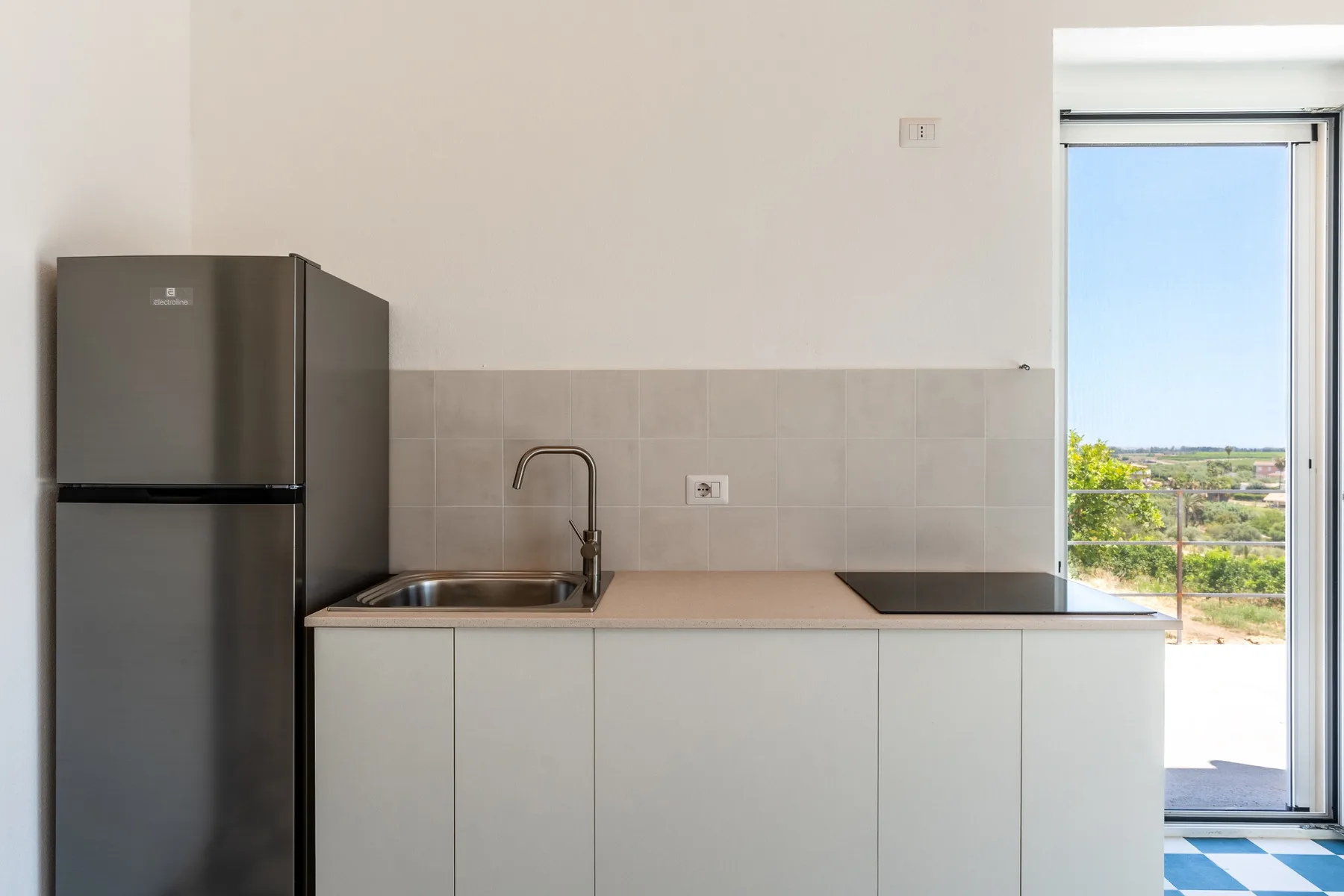 Una cocina compacta con refrigerador, fregadero y una puerta de vidrio luminosa.
