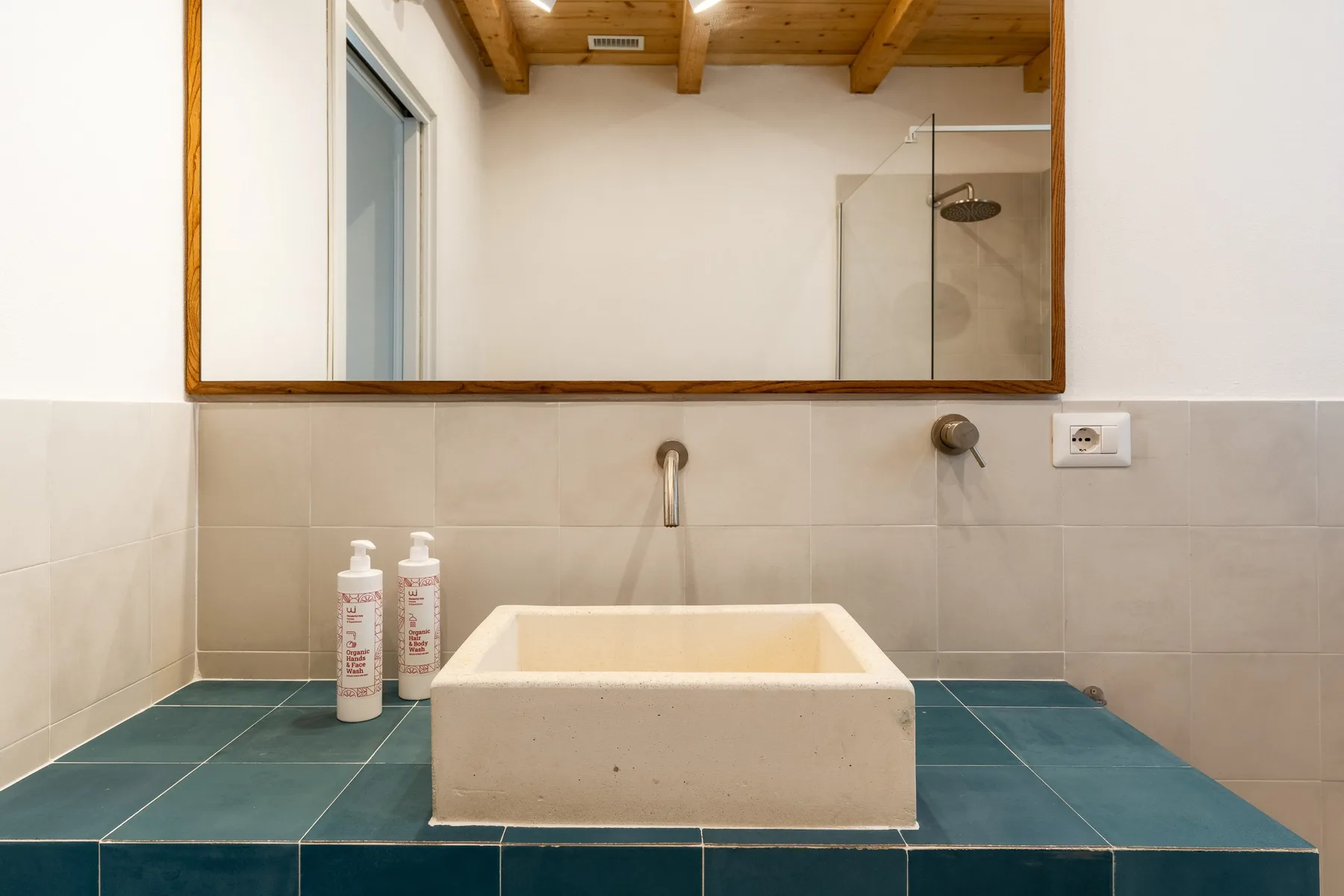 Un tocador de baño tiene un lavabo rectangular bajo un espejo grande.