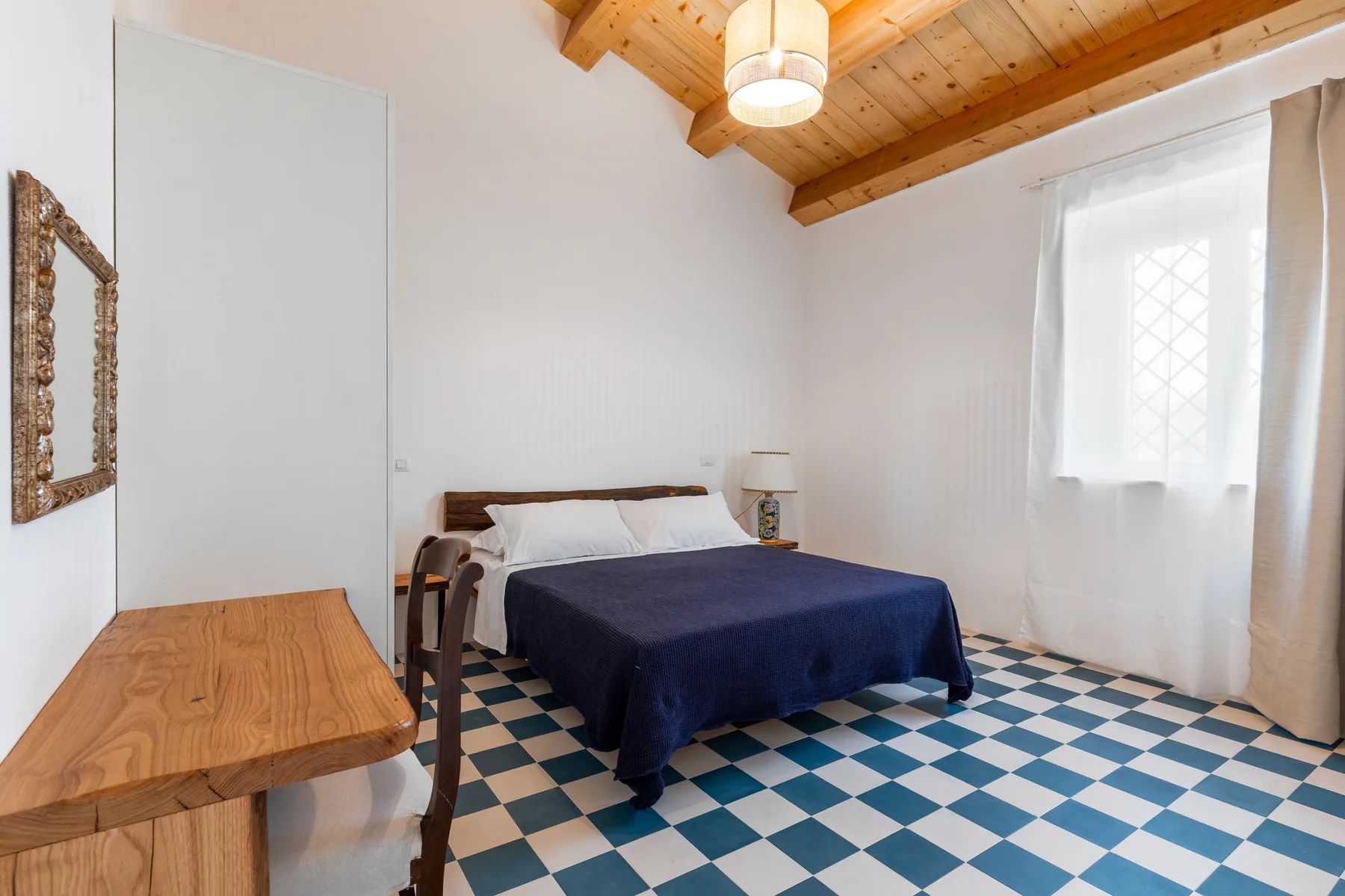 Un dormitorio con cama, techo de madera y suelo de baldosas azules y blancas.