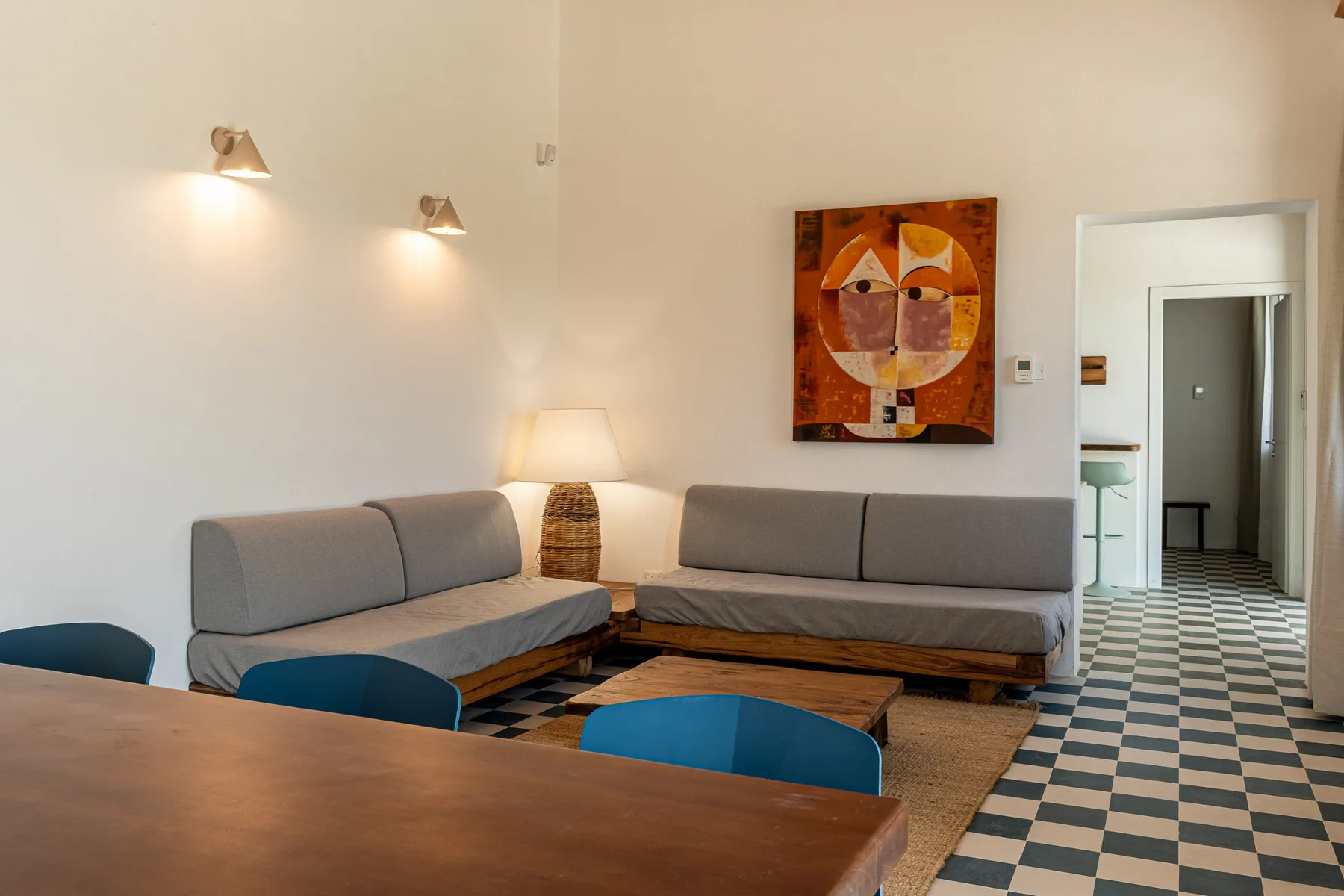Sala de estar con asientos grises, una mesa de madera y arte colorido en la pared.