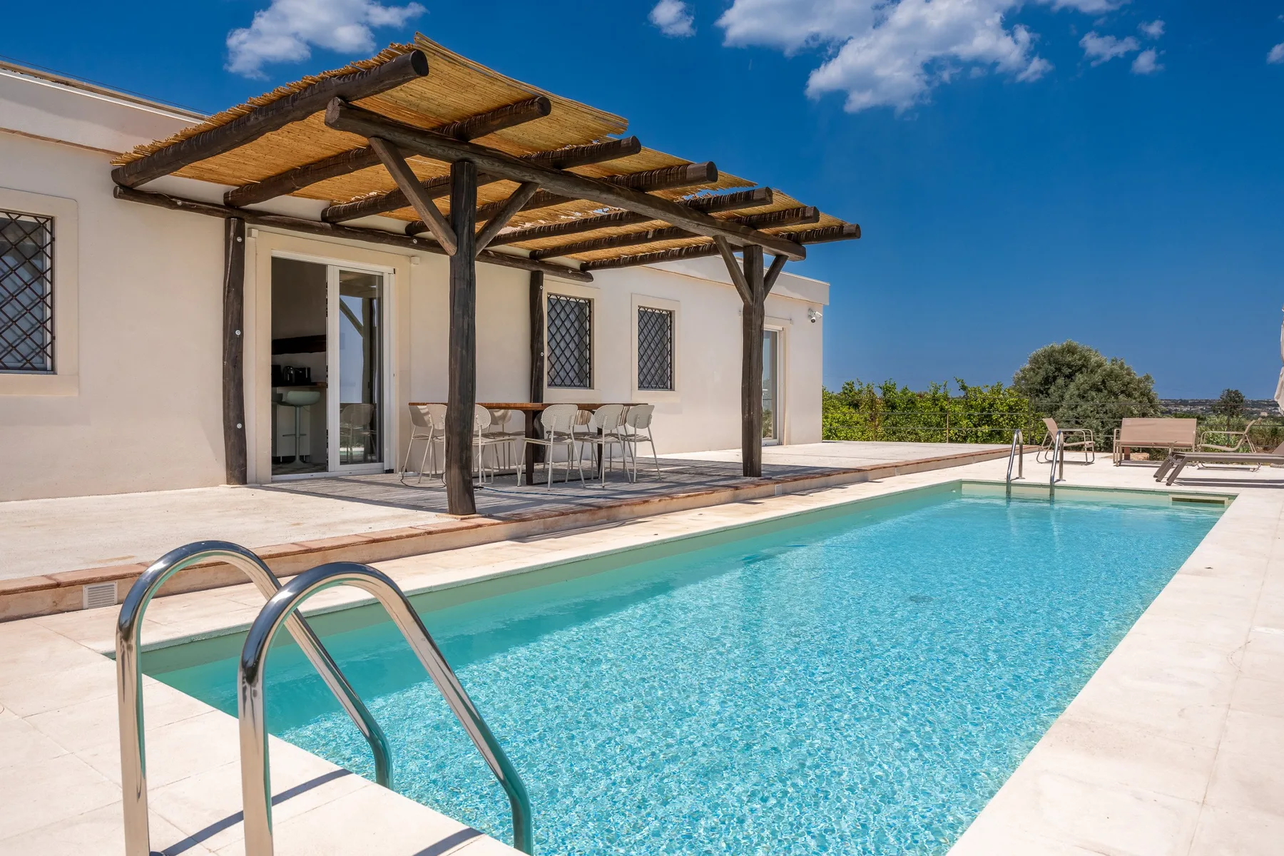 Una piscina al aire libre junto a una casa con un patio sombreado.