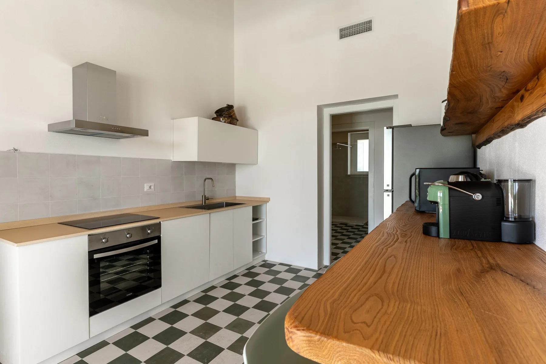 Una cocina con armarios blancos, suelo a cuadros y una encimera de madera.
