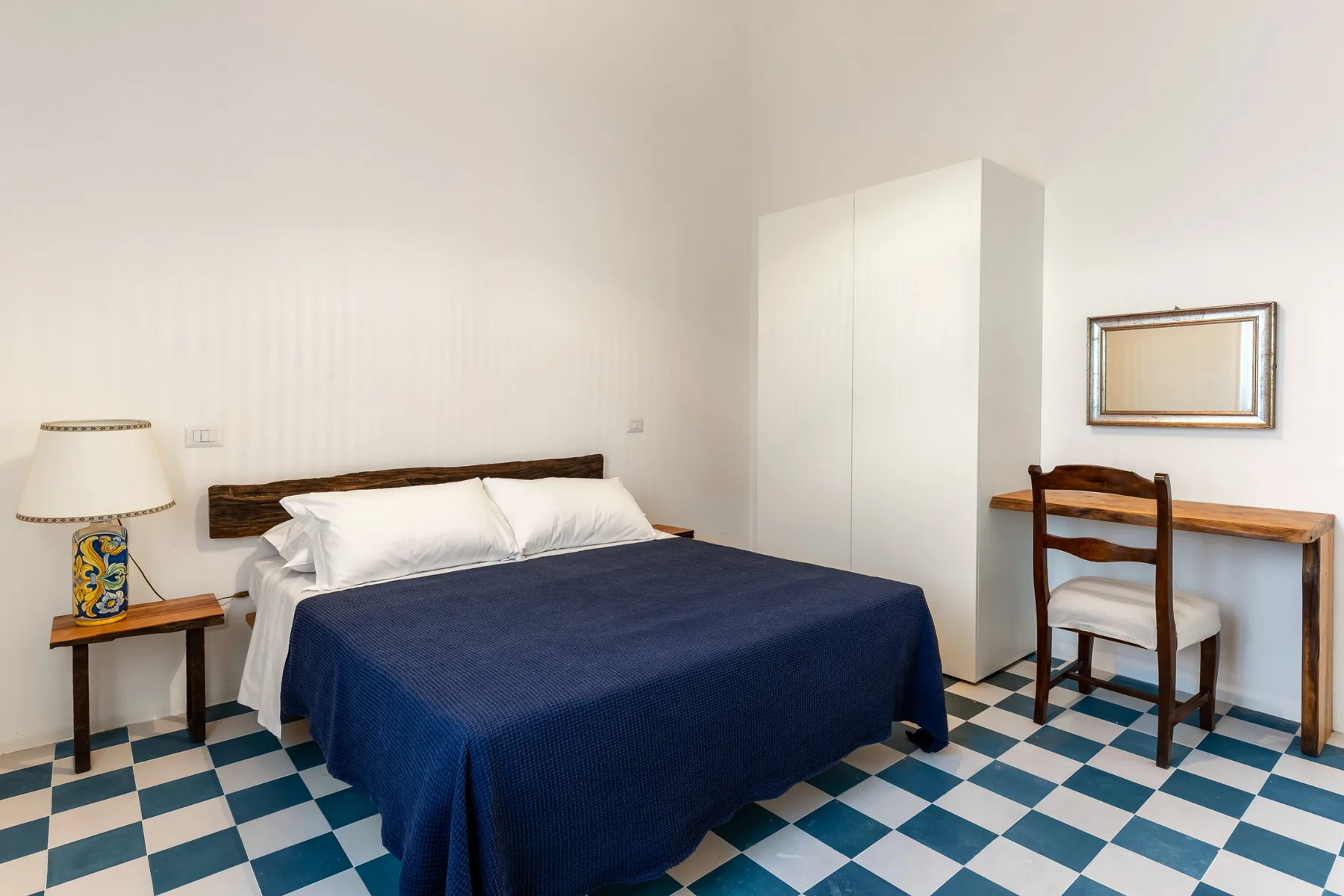Un dormitorio con una cama cubierta con una colcha azul oscuro y un pequeño escritorio.