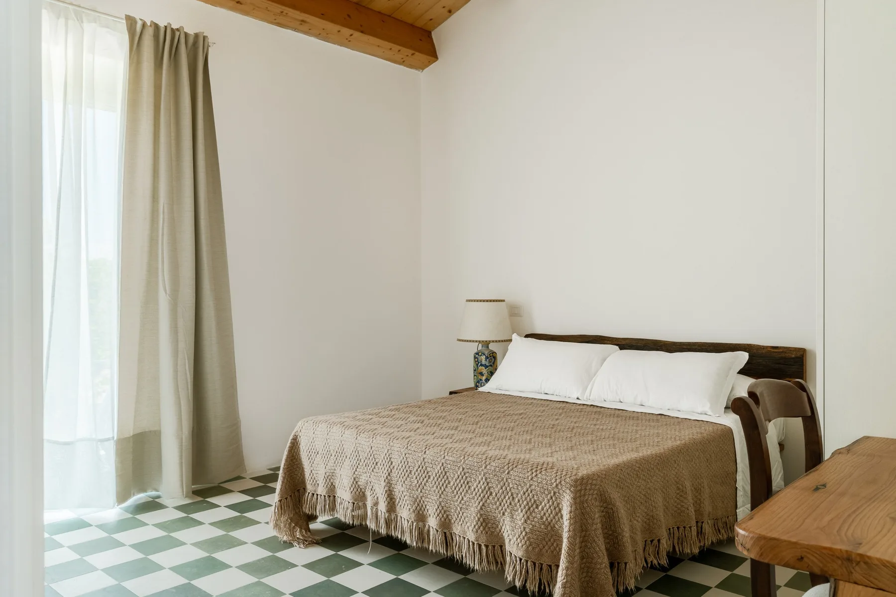 Un dormitorio con una cama tendida junto a una ventana con cortinas.