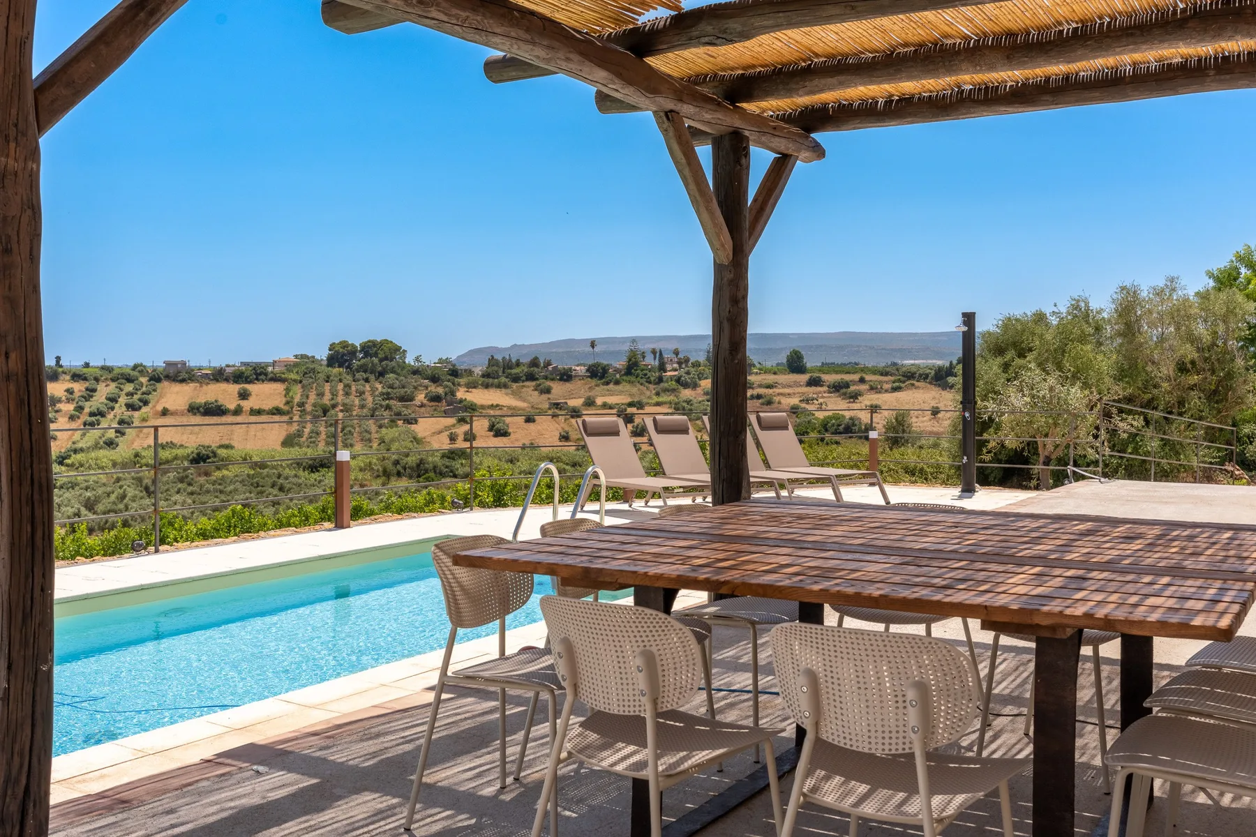 Una zona de comedor exterior a la sombra da a una piscina y al campo abierto.