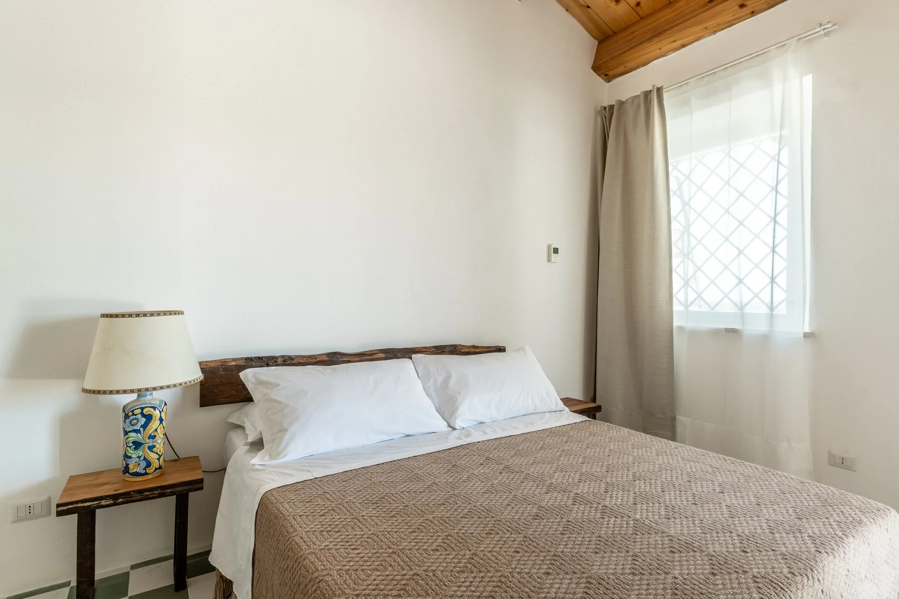 Dormitorio con una cama junto a una ventana con cortinas.