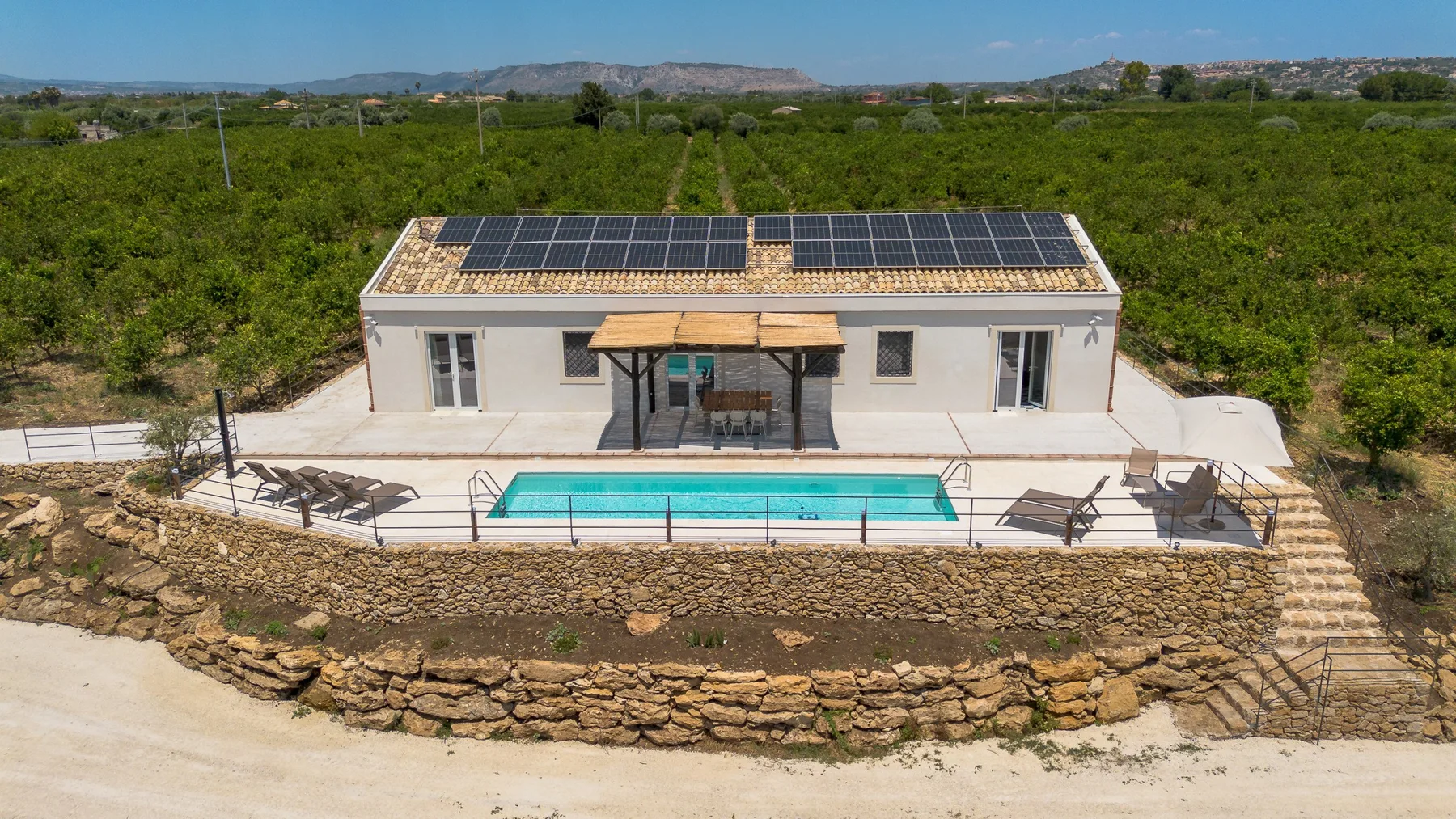 Una casa moderna con paneles solares da a una piscina y vegetación circundante.