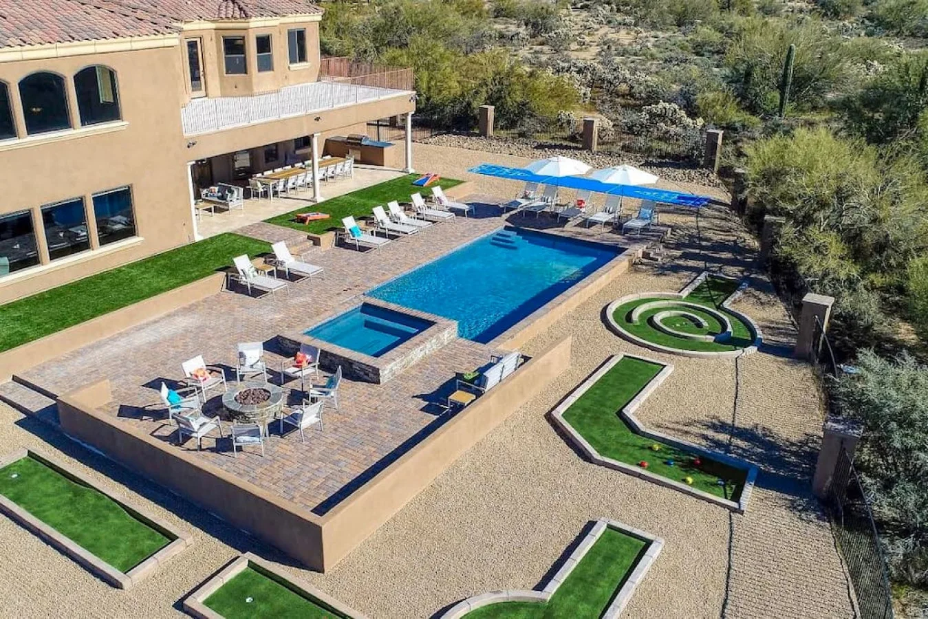 An outdoor pool and paved patio beside a large house, with landscaped garden beds.