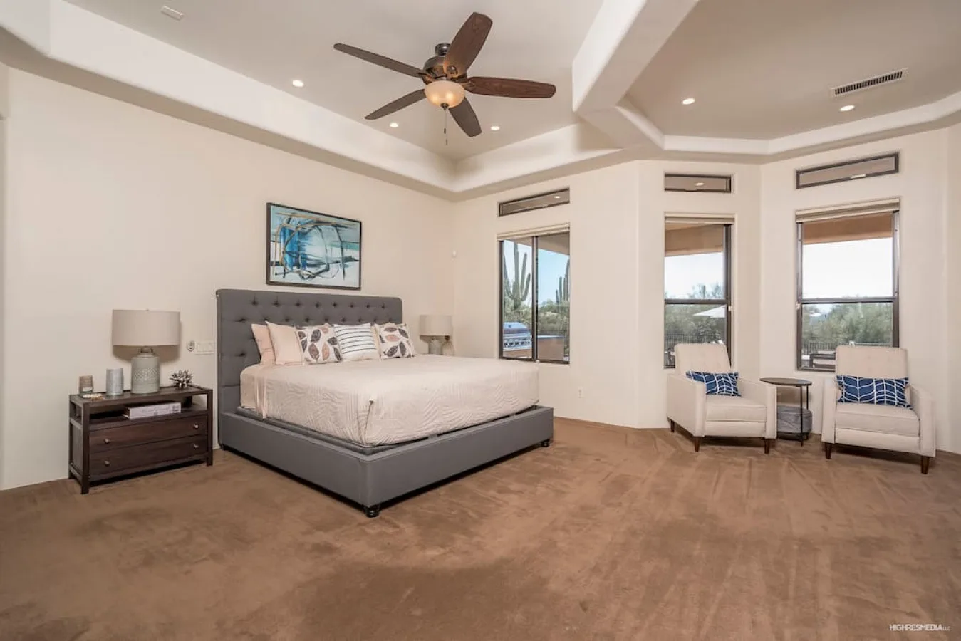 A spacious bedroom with a bed, bedside table, and seating by the windows.