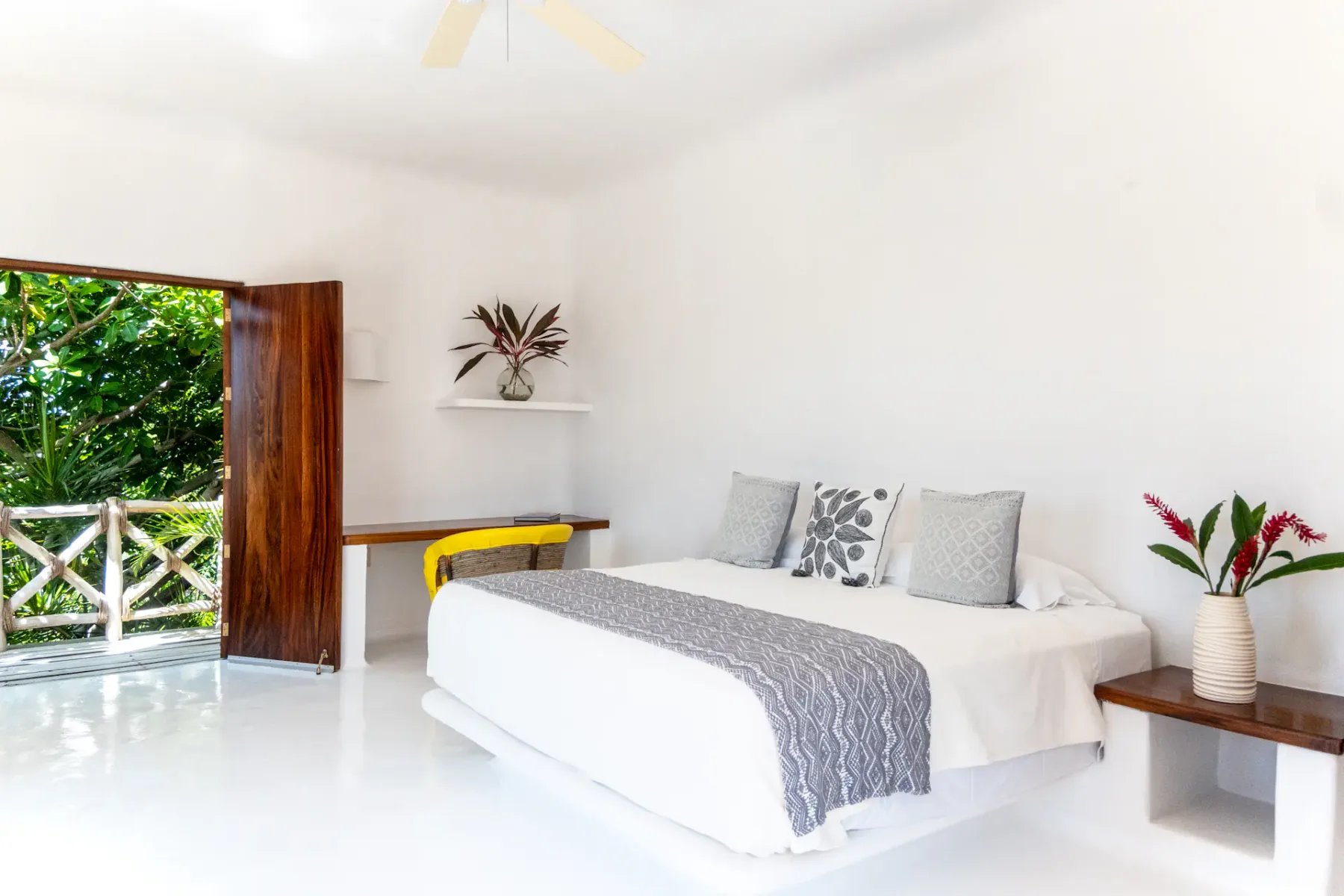 Un dormitorio luminoso con una cama blanca y una puerta de madera abierta hacia la vegetación.