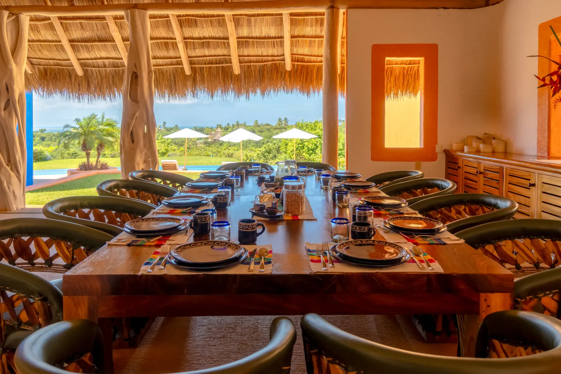 Comedor con una mesa larga preparada para comer y abierto a un jardín tropical.