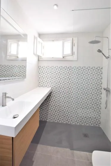 Un baño luminoso con un mueble de lavabo largo, azulejos estampados y una ducha.