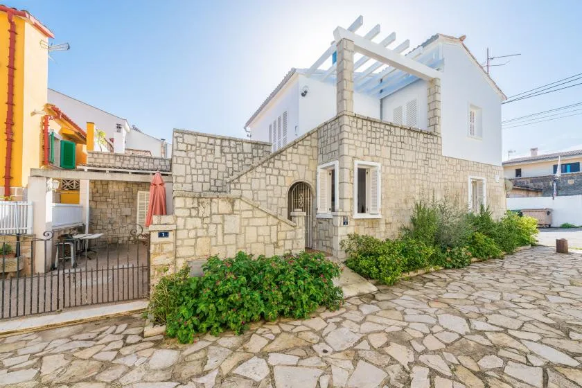 Una casa blanca con muros de piedra, una pérgola y un patio pavimentado.