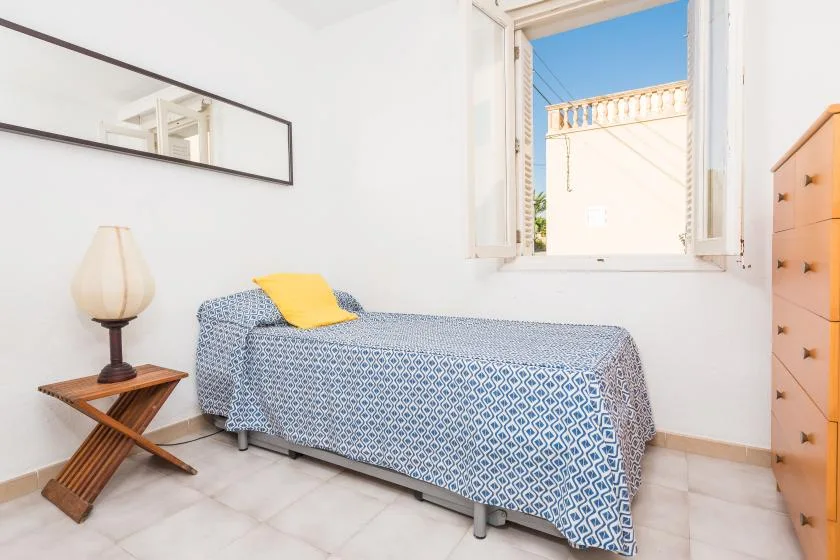 Un dormitorio luminoso con una cama individual junto a una ventana abierta.
