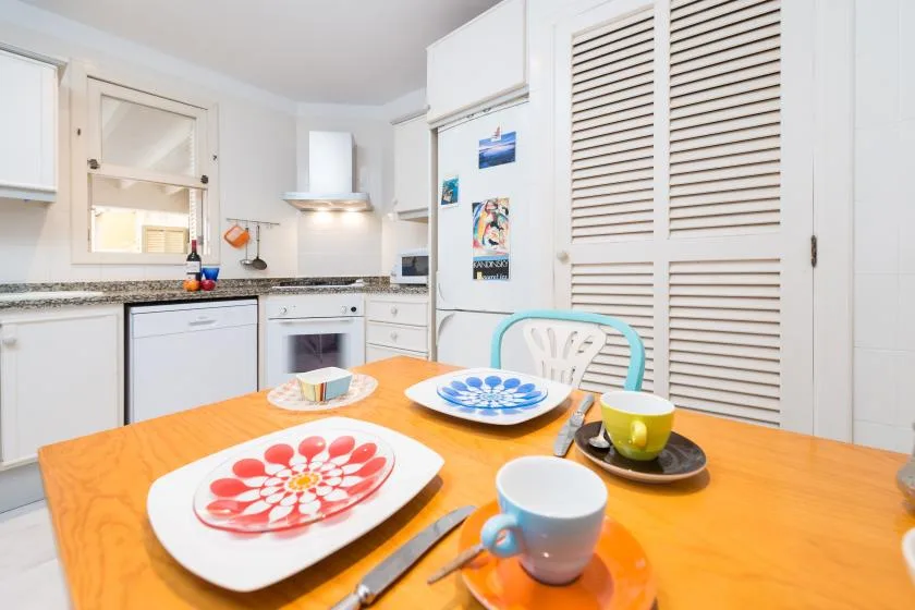 Una cocina luminosa con gabinetes blancos y una mesa de madera con platos.