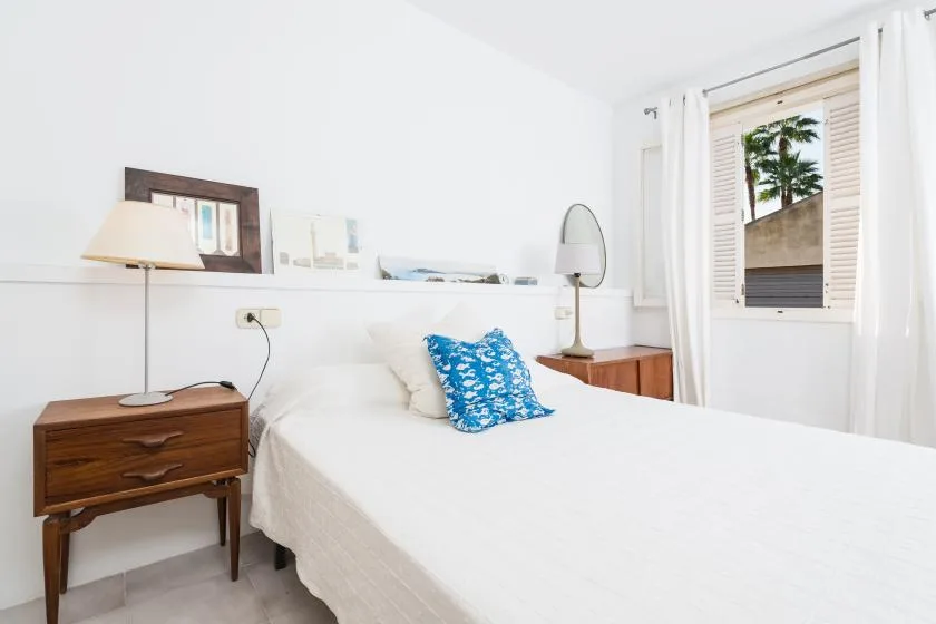 Un dormitorio luminoso con una cama, una mesita de noche y una ventana.