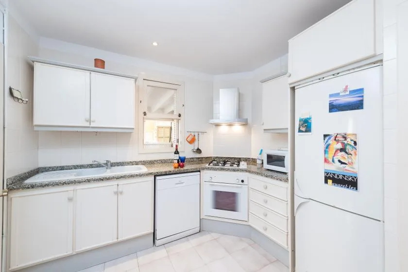 Una cocina blanca y luminosa con encimeras, una estufa y un refrigerador.