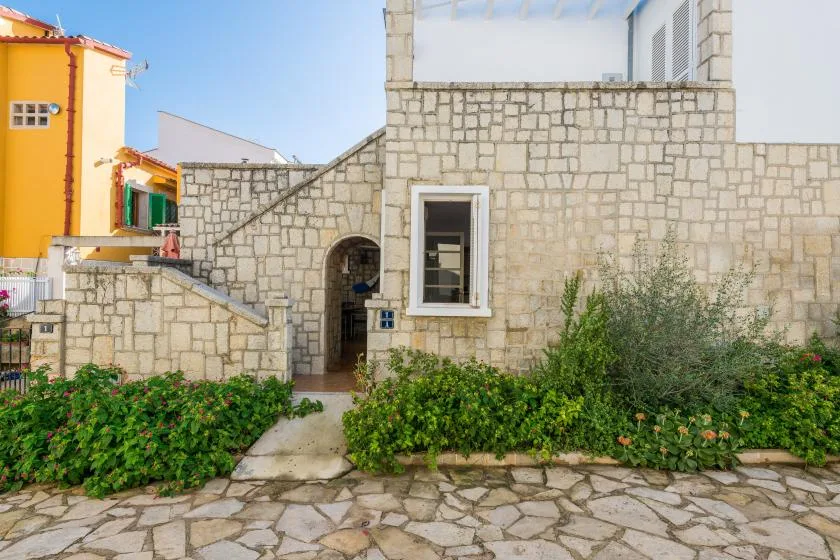 La entrada de un edificio de piedra da a un camino pavimentado bordeado de vegetación.