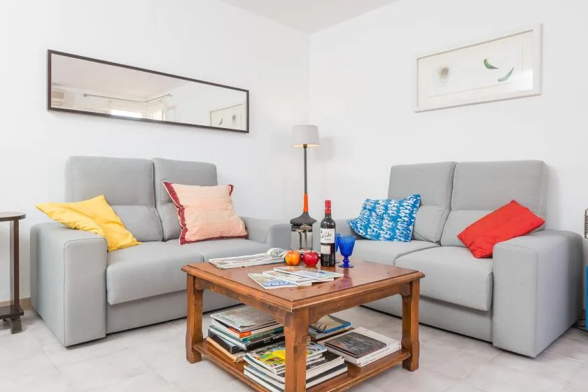 Una sala luminosa con asientos grises, cojines de colores y una mesa de centro de madera.