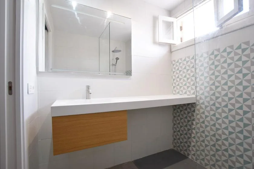 Un baño luminoso con una encimera larga y una pared de azulejos estampados.