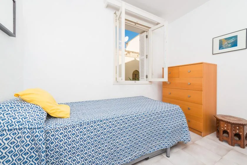 Un dormitorio con una cama estampada, una ventana abierta y una cómoda de madera.