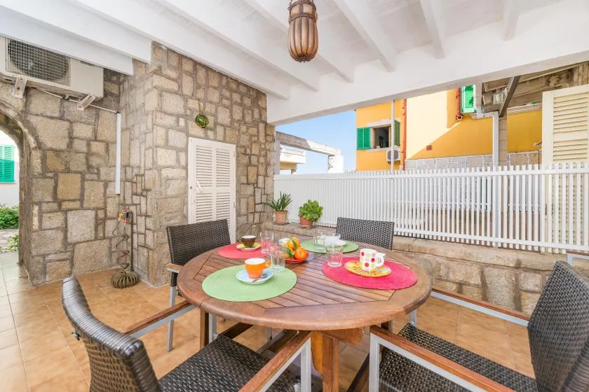 Un comedor al aire libre tiene una mesa redonda bajo un patio cubierto.