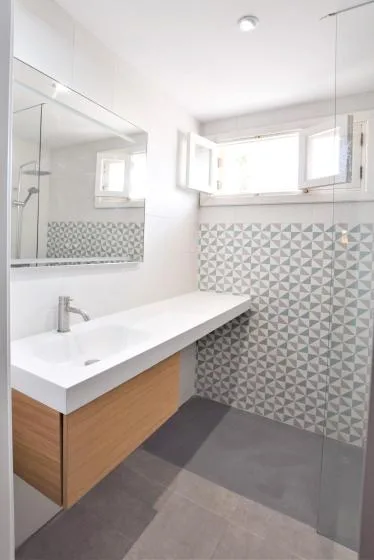 Un baño moderno con un lavabo blanco alargado, muebles de madera y azulejos estampados.